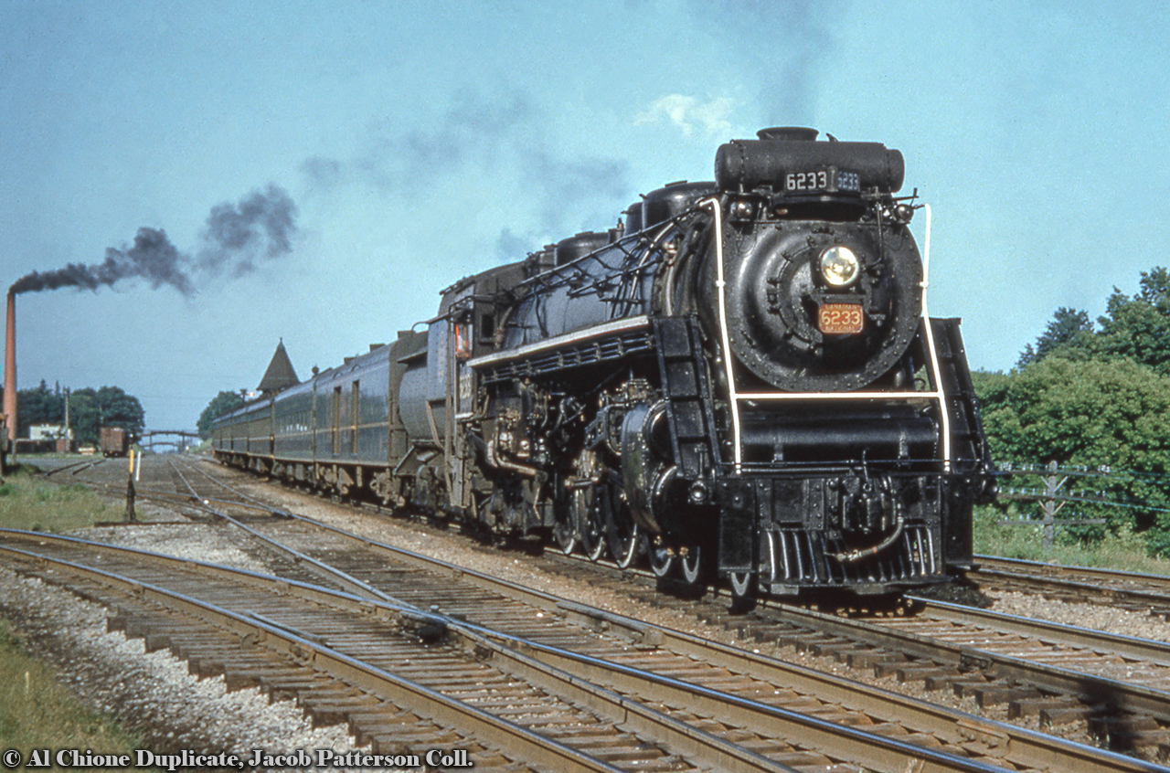 Westbound by Georgetown, CNR U-2-g 4-8-4 6233 (MLW, 1943) heads up Monday - Friday train 11 from Toronto to London, due into Georgetown at 1757h.  The foreground track curving of to the left is the northern section of the Milton Subdivision, running Georgetown to Allandale.  This would become the Beeton Subdivision in 1965 with the creation of the Halton Subdivision.In the distance at left is the former Georgetown Coated Paper Mills Ltd. building which had rail service.  Built in 1910, it would later become Alliance Paper Mills in 1928 before being purchased by Domtar in 1959.  It would carry the name Howard Smith Papers before becoming Domtar Fine Papers Ltd. until closing it's doors in 1978*.  The building survives today by as A-Plus Canada Inc Self-Storage and Applied Wiring Assemblies.  This Bill Thomson shot from 1965 shows the spur to the mill at right.  *Information from the Esquesing Historical Society.Original Photographer Unknown, Al Chione Duplicate, Jacob Patterson Collection.
