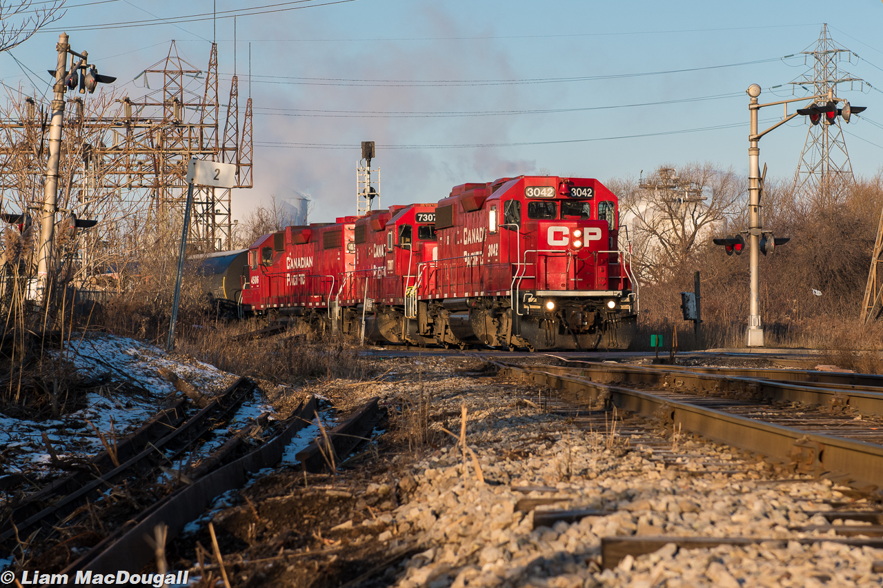 In some beautiful morning sunlight, CP TH11 is crossing Gage Avenue and the diamond with the CN N&NW spur with their cut of cars from Kinnear Yard. A trio of matching paint GP38-2s, each with different ownership history are the power.