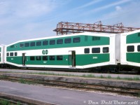 The big kahuna, the original, numero uno: the first car. GO Transit 2000, the first Bilevel commuter car built, sits in Willowbrook Yard adjacent to the canopy (that was under construction at the time). Sister cars 2003 and 2004 are coupled at either end, all part of the same original bilevel order that was less than a year old at the time. Note the neat stylized "HS" Hawker Siddeley Canada block logos on the ends of the cars.<br><br>Looking for a higher-capacity alternative to its <a href=http://www.railpictures.ca/?attachment_id=47228><b>single level cars</b></a>, and faced with the decision of running longer trains (and adjusting infrastructure to match) or higher capacity cars, in the 1970's GO Transit experimented with a few different commuter car designs, including borrowing both the <a href=http://www.railpictures.ca/?attachment_id=4062><b>C&NW gallery cars</b></a>, and the <a href=http://www.railpictures.ca/?attachment_id=21737><b>CP ones</b></a> built by Canadian Vickers. Not satisfied with the gallery car design, GO worked with Hawker Siddeley to make their own double deck commuter car design, dubbed the "Bilevel" commuter car, with two full levels in the middle and intermediate levels at each end, and two sets of doors to improve passenger flow.<br><br>The initial 1977 order was for 80 coach cars (2000-2079), and over four decades later GO has amassed a fleet of over 900 bilevels, including most of the originals. Subsequent orders included cab cars, and "accessible" cars with lower door controls (the initial conductors controls were located by the silver-framed upper sliding windows) and wheelchair ramps. The design changed hands over time, being first built by Hawker Siddeley Canada, then UTDC/Can-Car, Bombardier, and today Alstom Transport (all in the old Can-Car Thunder Bay, Ontario plant). Other commuter agencies also embraced the bilevel over time, and in recent years the design has had an upgrade with crumple zones to improve crash-worthiness, and a new cab car end design.<br><br>GO 2000 was one of 16 cars sold to Texas commuter startup Trinity Rail Express in 1997 (along with F59PH's <a href=http://www.railpictures.ca/?attachment_id=33769><b>565-568</b></a>) due to a mid-90's ridership decline, and became TRWX car 1050. The lowest-numbered bilevel on GO's roster today is 2002.<br><br><i>Original photographer unknown, Dan Dell'Unto collection slide.</i>