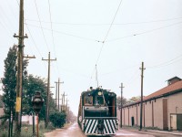 *** Submitted with the help of JACOB PATTERSON - Thank-you MIKE ***


The click of a shutter... and what do we have here... NS&T Electric Motor #21 travelling south on Elm Street approaching the Killaly Street intersection.  The train would soon pass the non-interlocked (flagged) industrial diamond for the Canada Cement company spur that connected the factory to loading docks on the Welland Canal.  The final destination for the train would be the Macey Yard Interchange with the CNR.  The train is hauling boxcars from Robin Hood Flour Mills.  The NS&T was the last railway to reach Port Colborne in 1911, and the construction of Robin Hood in 1940 created a significant source of Freight Revenue for the Company, enough to dedicate an Electric Motor to servicing the facility.  NS&T generally kept Motor #20 or 21 stationed adjacent the current Museum grounds.  #21 was built by the CLC - Canada Locomotive Company in 1927 for the Montreal & Southern Counties coming over to NS&T in 1941, likely due to freight demands at Robin Hood.  The building on the right was the privately built Port Colborne Athletic Club Arena (also called the White Arena), a 2200 seat hockey rink constructed in 1932 that launched the NHL career of of 5 time Stanley Cup Champion- Toronto Maple Leafs Captain - Ted "Teeder" Kennedy who joined the Leafs at age 16.  According to the NS&T author John Mills the last Interurban Trolley passenger run in North America was Thorold to Port Colborne - March 1959.  Electric Motor freight operations continued until the summer of 1960 at which time the line was serviced by Diesel locomotives.  Street running to the Robin Hood terminated in 1983 (or '84) when the tracks were removed as the line was re-routed from Welland south to Robin Hood and the then new "Canada Starch" plant.  The scene looks very much different today, the Cape Cod style homes on the left are still there, the rink was demolished in the late '60's, streets widened and gentrified.  