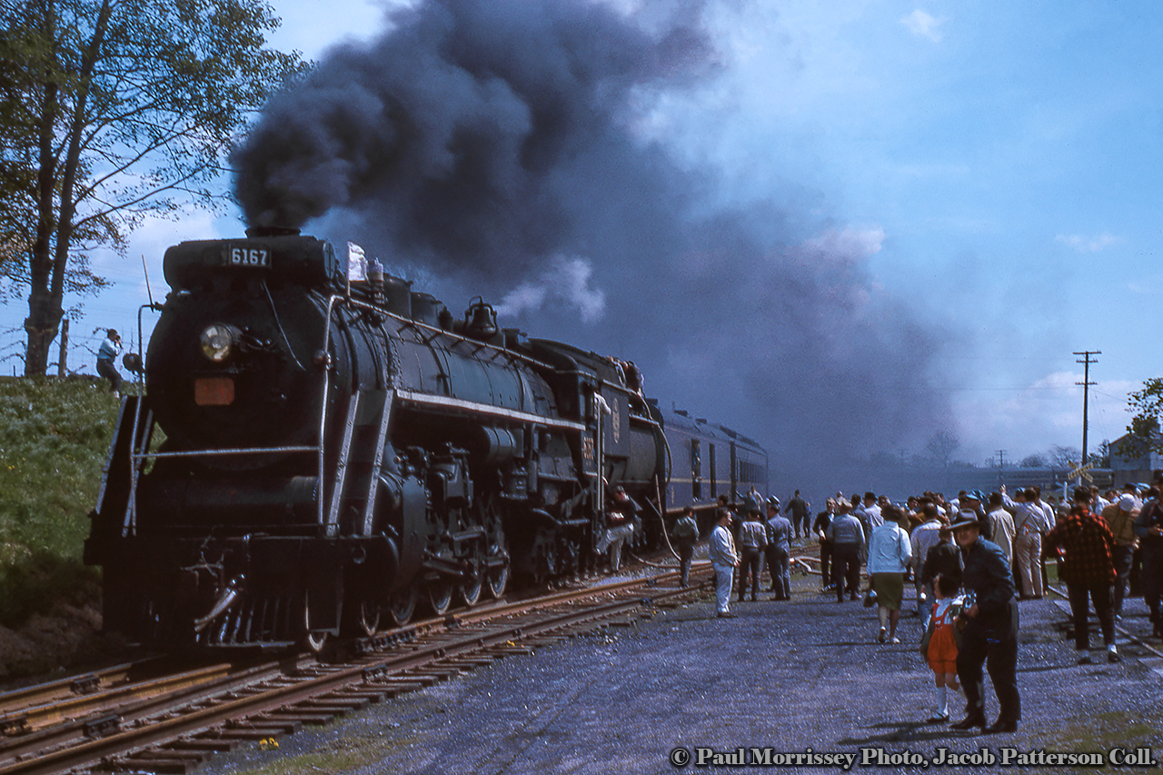 With 16 months left before retirement in September 1964, Canadian National Railways 6167 is seen smoking it up during its excursion career, pausing for water at Caledonia at the corner of Inverness Street and Orkney Street West (note crossbucks at right) in May 1963.  Today 6167 is on display at Guelph as part of the Guelph Museums' collection.  Recently the locomotive's tender was coupled to the locomotive after sitting separate since the move to Priory Park in 2020.  New windows and a coat of paint are planned in the near future.Paul Morrissey, Jacob Patterson Collection Slide.