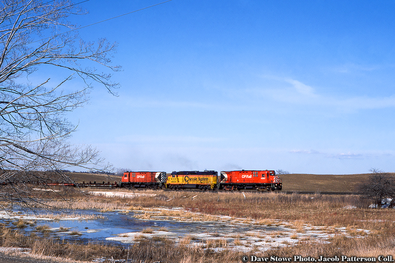 The other Copetown.  The CP Rail operation of the Nanticoke steel train rumbles westbound along the Waterford Subdivision at Copetown, passing the muskeg ponds approaching the Highway 52 crossing near Powerline Road.  Power includes a pair of MLW C424s bracketing the leased Chessie (B&O) GP38 4806.Built by MLW in 1965, both C424s would be retired in the late 90s, with 4207 retired in 1996 and sold to Century Metals of Lachine, Quebec for scrap in 1997, and 4227 sold to HELM in 1997 for refurbishment and future sale to the Apache Railway.  It was still in operation as recently as 2018 as their 98.  B&O 4806, built 1970, has had a number of owners and numbers, starting with CSXT 2106, to Grand Rapids and Eastern Railroad 5106, renumbered to GR 3839, and now operating for the G&W family on the Mid-Michigan Railroad as the 2057.,A few days before on March 27, Robert Farkas snapped this power at Chatham Street roundhouse, and it appears Doug Page also shot the run above over at Aberdeen Yard before departure.Dave Stowe Photo, Jacob Patterson Collection Slide.