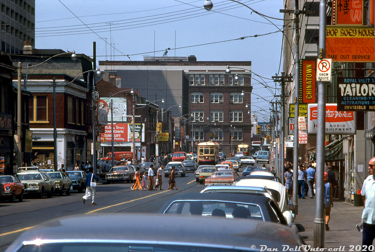 One for the 70's automotive enthusiast: TTC Peter Witt streetcar 2766 trundles down Dundas Street in Tour Tram service, during a warm bustling Summer afternoon in downtown Toronto. This telephoto image was shot looking west on Dundas from Bay towards University Avenue in the distance (the big brown building was originally the Ontario Veterinary College, later The Province of Ontario Savings Branch). 

Street signs, many advertising Chinese businesses, jut out from streetside storefronts along Dundas Street. This area used to be Toronto's old Chinatown, but due to nearby development of the new City Hall in the 60's (that expropriated many buildings to the south along Elizabeth Street in "The Ward") many of the Asian-run businesses moved to a "new" Chinatown focused around Spadina and Dundas.

Original photographer unknown, Dan Dell'Unto collection slide.