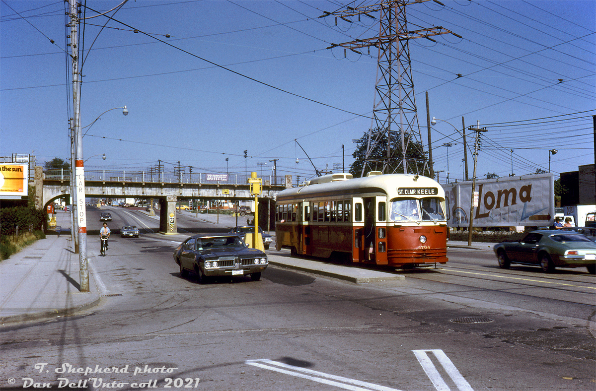 During her last year in service, TTC PCC 4764 (an A14-class car built in 1946 by St. Louis Car for Kansas City, Missouri) pauses along the St. Clair route at the platform stop at Prescott Avenue, just west of the 1931-built CN Newmarket Sub bridge.Pre-1931, the CN Newmarket Sub crossed St. Clair Avenue here at-grade, and streetcars terminated at loops on either side of the crossing, necessitating riders to de-board, cross the tracks, and board another streetcar to continue further (the Dovercourt streetcar terminated here at the west side at Prescott Loop, and the St. Clair car terminated on the east side at Caledonia Loop). The construction of this bridge/underpass/grade separation in 1931 (and re-alignment of the Newmarket Sub, and new CN St. Clair Avenue station) allowed the St. Clair streetcar tracks to join and eliminated all the inconvenient loops and transfers for passengers.The TTC's A14 ex-Kansas City cars were some of the first secondhand PCC's to leave the roster due to lackluster maintenance from their original owner. Car 4764 was one of 11 sold to MUNI in San Francisco to operate until their new cars were delivered. Renumbered 1184, she never ran in service and was reportedly used as a parts car.T. Shepherd photo, Dan Dell'Unto collection slide.