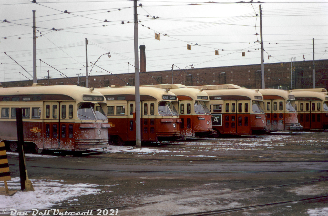Various flavours of Toronto Transit Commission PCC's crowd the yard tracks of Roncesvalles Carhouse on a wintery day in early 1973, waiting their next trip out on routes such as King, Queen, and Carlton that were run out of Roncesvalles (Roncesvalles on the destination roller blind instead one of the usual endpoint usually meant a car was short-turning or going out of service at that street, and returning to the carhouse). From left to right are an A6-class car (43xx), A7 (4400), two ex-Cleveland A11's (46xx, the first fully repainted in subway red), another A6 (recently rebuilt and sporting a water bumper) and an A7. Couplers on some cars (44xx (A7) and 46xx (A11)) were for MU service on the busy Queen route. Road salt and brine coat a few of the cars that have been out in service, others have recently visited the wash rack and are a bit cleaner. Needless to say, decades of winter service on Toronto roads did not bode well for the condition of many cars at the ends of their service lives.Original photographer unknown, Dan Dell'Unto collection slide.