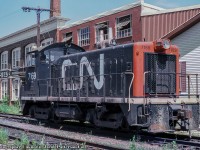 The CN Guelph yard power is seen parked in track XW41, the southernmost track across from <a href=http://www.railpictures.ca/?attachment_id=47517>CN's Guelph station.</a>  Power is CN 7169, an 800hp GMD SW8 built in 1951, originally one of the 34 SW8s numbered in the 8500 - 8533 series prior to 1956 renumbering to 7150 - 7183.  All would be off the roster by 1989.<br><br>Behind the unit sits two buildings, an older wood and timber structure at right at 72 Farquhar Street, and the brick factory on the left at 76 Farquhar Street, both part of Guelph's textile and agriculture history.  The "medium" structure at centre was an addition during the 1920s to connect the two main buildings.  At right, Guelph's Drill Hall built 1866 served the military for practicing various drills until the 1890s.  <a href=https://www.historicplaces.ca/hpimages/Thumbnails/70544_Large.jpg>The armoury</a> would not be built until 1906, directly across the street and still in use today.  The site first became part of Guelph's textile manufacturing sector in the early 1890s as part of the shirt making company, Williams, Green & Rome, per an 1892 fire insurance map.  By the early 1900s the factory at left had been built and the full site was in use as the Guelph Cotton Mills per a 1907 fire insurance map, and by 1908, taken over by the Louden Machinery Company (the word "Louden" barely visible <a href=https://s3.amazonaws.com/pastperfectonline/images/museum_51/155/201484416.jpg>in this 1908 photo</a>) for the manufacturing of agricultural equipment.  The Aspinwall Manufacturing Company would assume operation of the site in 1912 as their only Canadian plant <a href=https://s3.amazonaws.com/pastperfectonline/images/museum_51/091/2009321996.jpg>(seen here circa 1915)</a> making equipment for potato farmers, including their automated potato planters, sprayers, cutters, sorters, and weeders.  Some examples <a href=https://scontent-yyz1-1.xx.fbcdn.net/v/t1.6435-9/91737493_1504970392986148_3226917549207715840_n.jpg?_nc_cat=102&ccb=1-5&_nc_sid=730e14&_nc_ohc=2nN2XysgxDQAX_UgwhA&_nc_oc=AQnFxjwNN1a4bhF5-7t-bU4C5P4Kqvd9mTo6-yK0V4MPyk9t-R2VUShIa78zB8Gpofo&_nc_ht=scontent-yyz1-1.xx&oh=00_AT_uWrdIHK5pJ1gySdSnMa0eTfTh0E7IpYXpxbVH9cK0nA&oe=61F528B3>of their equipment seen here.</a>  Per a 1929 fire insurance map, the properties were once again in the textile industry under the Regent Knitting Company, and later by Zephyr Looms and Textiles Inc. in the late 1930s.  Zephyr Looms & Textiles worked through the Second World War handling military contracts for uniform articles and other small items.  Emerging from the war, the company would rebrand as Textile Industries Ltd. in December 1945, which it would operate as until closing for good in December of 1980.  At some point during the 1970s a slight change in the name recognized their location in Guelph on Wyndham Street, as they became known as <a href=https://s3.amazonaws.com/pastperfectonline/images/museum_51/061/199228190.jpg>Wyndham Textile Industries Limited.</a><br><br><i>Original Photographer Unknown, Jacob Patterson Collection Slide.</i>