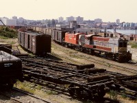 One year and four days after this everyday view from the sand shed roof in Victoria on Thursday 1972-06-08, lead unit 8007 on this train was severely damaged (along with three other Baldwins) in a head-on collision a bit south of Nanaimo.  Second unit 8002, which for its slightly sharp distinct M-3 horn was a favourite of mine, survived to the March 1975 end of Baldwin roadswitcher operation on the E&N.

<p>In the foreground, the de-bunked open-deck log cars are in for scrapping, with the removed bunks being utilized to ready steel-decked flatcars for Lake Cowichan log service.  On the far left, the tender is for the auxiliary crane then still very active at Victoria.  It was practically a working museum there.

<p>In the background, above the engine hood of the lead unit, the Island Tug & Barge rail-car slip for direct interchange connections to USA ports can be seen.