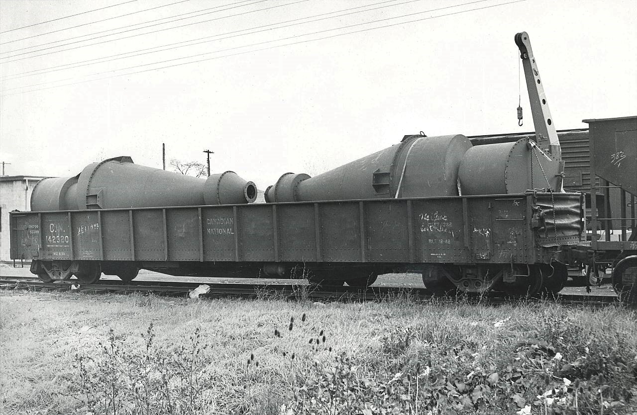 Completed "Cyclone Separators" have been loaded into Gondola 142320 on the spur that lead through the Sherk Lumber property to the rear (north side) of Port Colborne Iron Works / E.B. Magee, a custom fabricator, boiler  shop and sometime Great Lakes ship builder.  Cyclone Separators are generally used in dust / pollution control applications and would have been considered newer / greener technology at that time.  It appears that the spur had at least 2 tracks with the mobile crane parked between the gon and the steel boxcar.  142320 was built in Dec 1942 and is a riveted steel construction.  The gon looks to be labeled both "Welland" and "Magee" (illegible) on the east and west ends respectively.  The Port Colborne Iron Works closed in the early 2000's, and the current building occupant is an unrelated company, LA Steel.  The spur to the plant through Sherk Lumber was removed in/around the time PC Iron Works ceased operations.