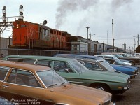 CN RS18 3151 works a westbound VIA Tempo train, smoking it up it (along with the HEP baggage generator car) as the train pulls out of Burlington West station past the parking lot. An assortment of 70's automotive iron in the in-colours of the day are parked along the fence line, likely belonging to VIA and GO riders away at work in Toronto and other points along the line.
<br><br>
<i>Keith Hansen photo, Dan Dell'Unto collection slide.</i>