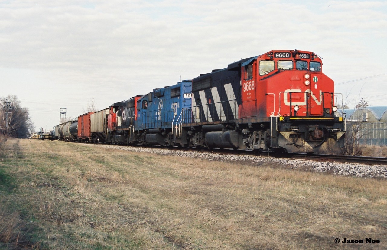 CN 421 has just crossed Strange Street in Kitchener as it heads westbound to Stratford with 9668, EMDX 806 and 9508 after lifting and setting-off at the yard. In the background the tower from the Epton Industries Inc. plant at King Street is seen above downtown Kitchener. Later that summer, the company would announce bankruptcy and in turn cease plastics production, eventually closing the facility by December 31 that year, after failing to meet a payment plan.