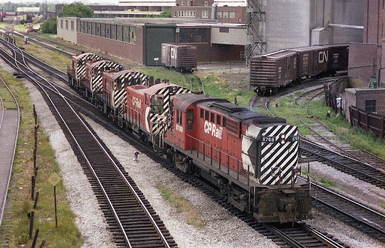 This image is of a CP power move that came up from Parkdale and heading west on the Galt sub, as seen from the old Weston Road bridge. Power visible is CP 8768, 8146, 7043, 7060 and 7024.  The three 7000-series MLW S-2 switchers were all retired by 1986. On the north (upper) side can be seen two leads to the Maple Leaf Mills plant as well as a one to a warehouse.  Most all of this industrial area has been demolished beginning 1992 or so and has been replaced by condo towers. This view is but a few hundred yards west of the old classic West Toronto Diamond; a hangout for many of us in the days gone by.  Now? Fergit it.