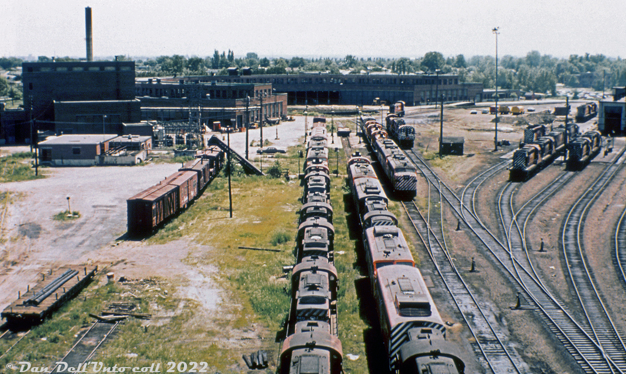 The 1975 traffic downturn that sidelined CP's fleet of CLC and Baldwin locomotives also sidelined much of the 244-powered Alco/MLW fleet as well, including the entire fleet of FA/FB cowl-bodied units. Viewed from the coal tower, lines of stored CP MLW units fill the shop tracks by St. Luc roundhouse, including FA1/FB1, FA2/FB2, FPA2/FPB2, RS3 and RS10 units with stacks capped. The B-units were rounded up first, and the last active FA, 4089, would be shoved into the deadline in November 1975.  The more modern St. Luc diesel shop is shown on the right, with C424's, RS18's (251-powered units were spared) and SD40-2's. Some switchers are parked on a track adjacent to the deadlines.  While most of the stored RS3's and RS10's would be reactivated and put back to work for a few more years, the FA/FB fleet would remain stored until official retirement in 1977 and subsequent scrapping. Two units would be set aside for preservation (4090 & 4469). One unit would be converted into an air repeater car (4085 to 1100). A handful of B-units would be de-engined by Angus Shops, renumbered as AN-xx units, and stored again as potential fodder for conversion into robot/radio control cars for Locotrol use out west (only one would ultimately be converted, 4463 to RCC-5 (2nd)).  Left side from close to far: 8472, 8567, 8482?, 8467? (M&G paint), RS3, FA1, FA2?, baggage car, caboose Right side from close to far: 4409, 4019, 8582, 4467, 4092, RS3 Upper right side: FPA2, FA1, FB2, URS RS3's 15-17, FB2?. Original photographer unknown, Dan Dell'Unto collection slide.