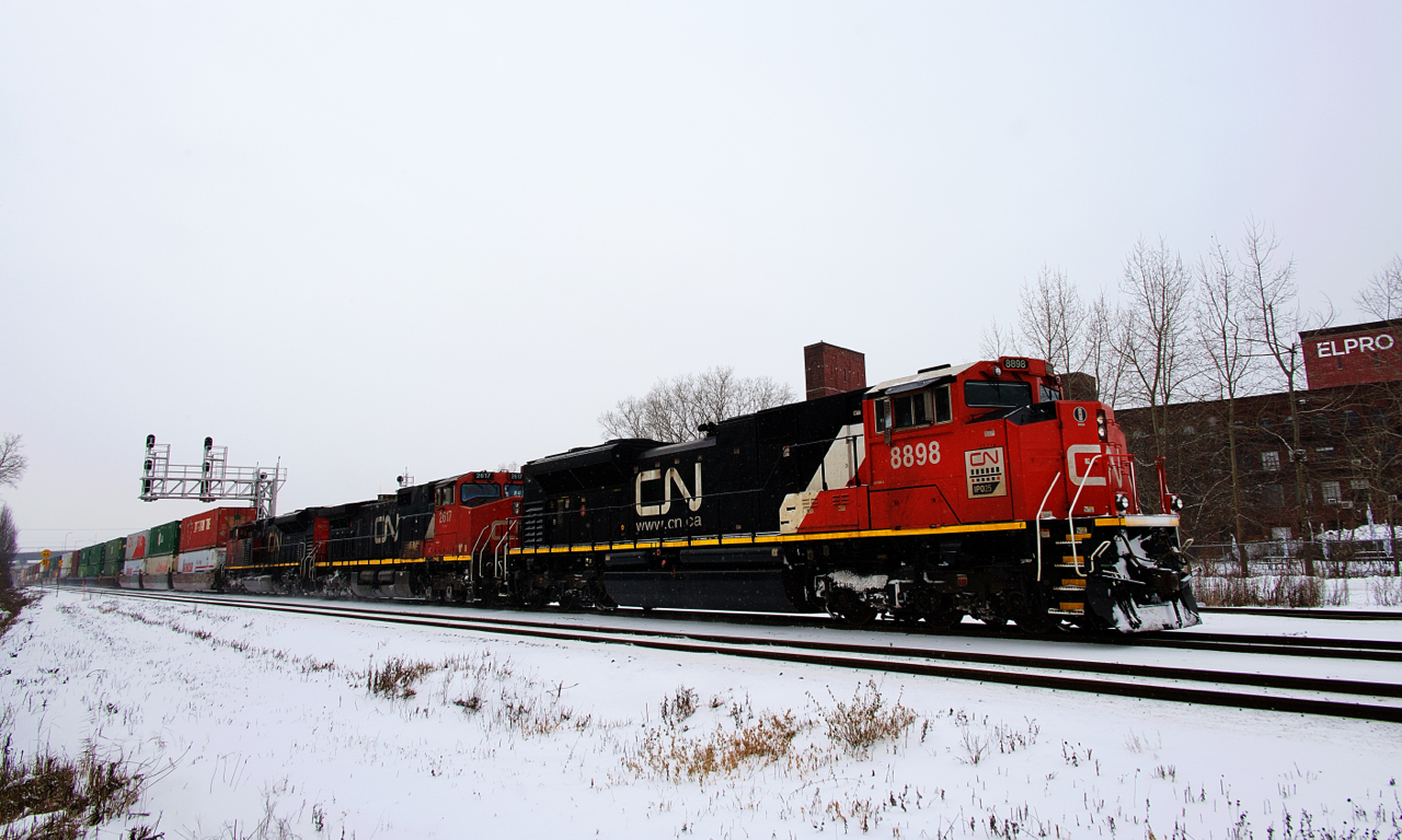 CN 8898 has a sticker on its nose commemorating the 25th anniversary of CN's initial public offering as it leads a 600-axle long CN 120 through the snow.