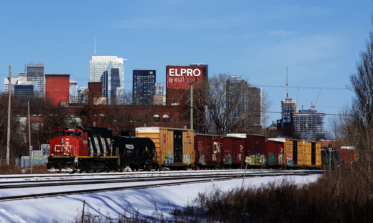 The St-Hyacinthe Switcher (CN 519) is unusually seen in Montreal, passing the skyline of the city with CN 9454 and about 60 cars to leave on Track 29 of the Montreal Sub.