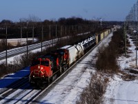 CN 369 heads west with CN 2561, CN 8875 and 124 cars on a frigid winter day. In the distance, counterpart CN 368 is lined on the north track and beyond that, the headlight of CP F95 is barely visible.