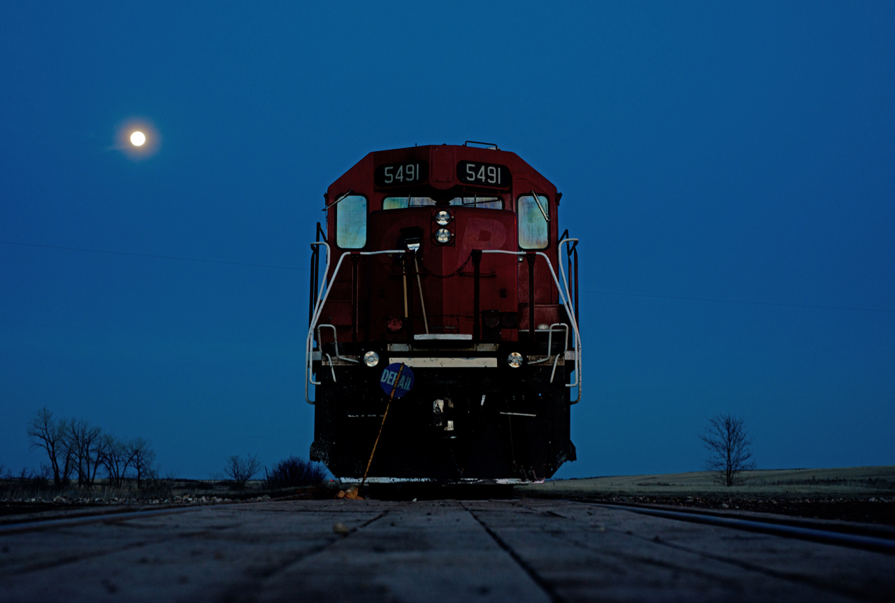 Last Mountain Railway sits tied down on the main in the town of Findlater under a full moon.  The portable derail is brought along and used where ever the crew runs out of time.