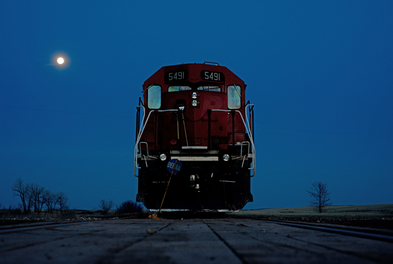 Last Mountain Railway sits tied down on the main in the town of Findlater under a full moon.  The portable derail is brought along and used where ever the crew runs out of time.