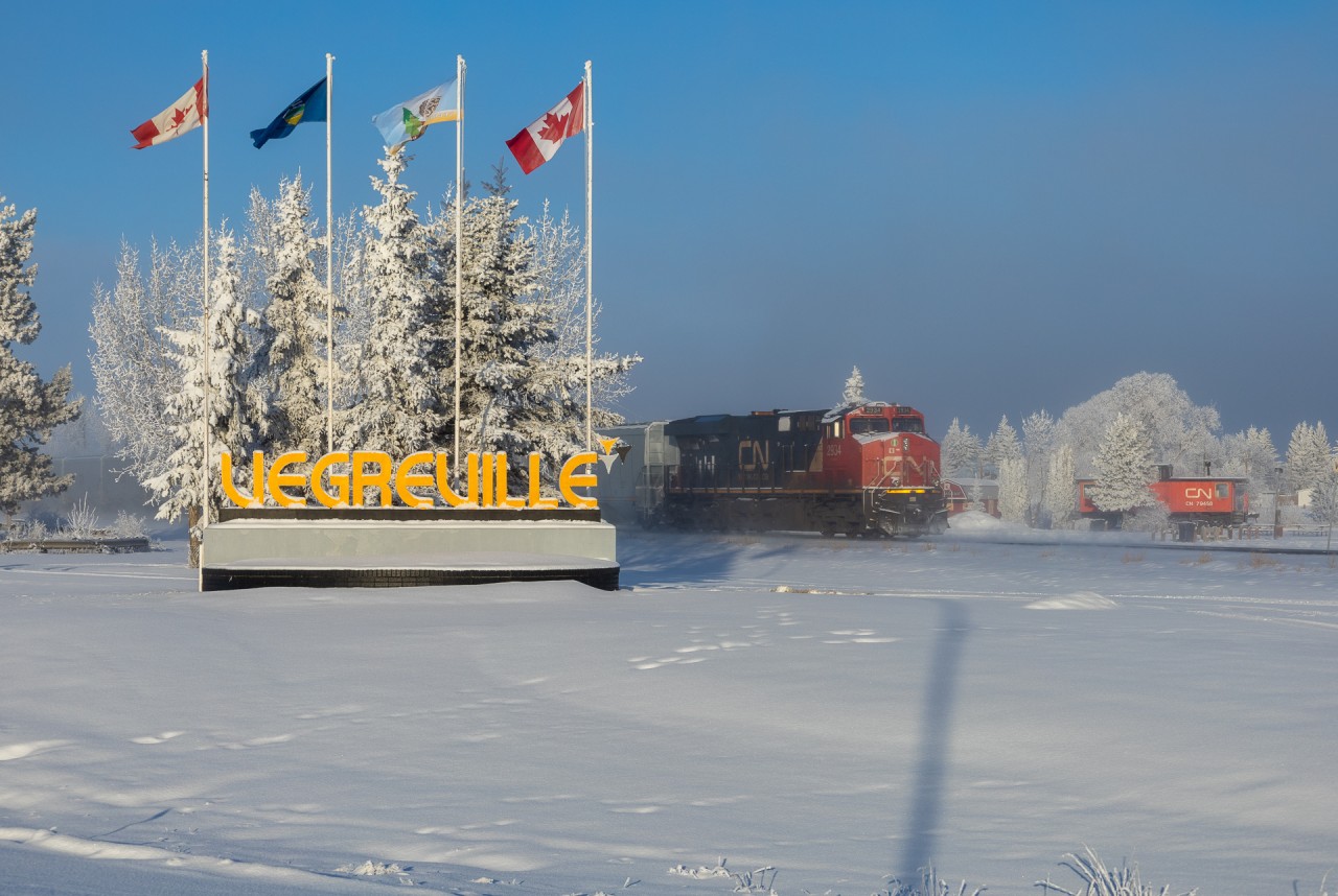 CN 2934 shoves hard on the tailend of G 24351 11 passing an old CN Caboose at the Vegreville Visitor Information Centre
