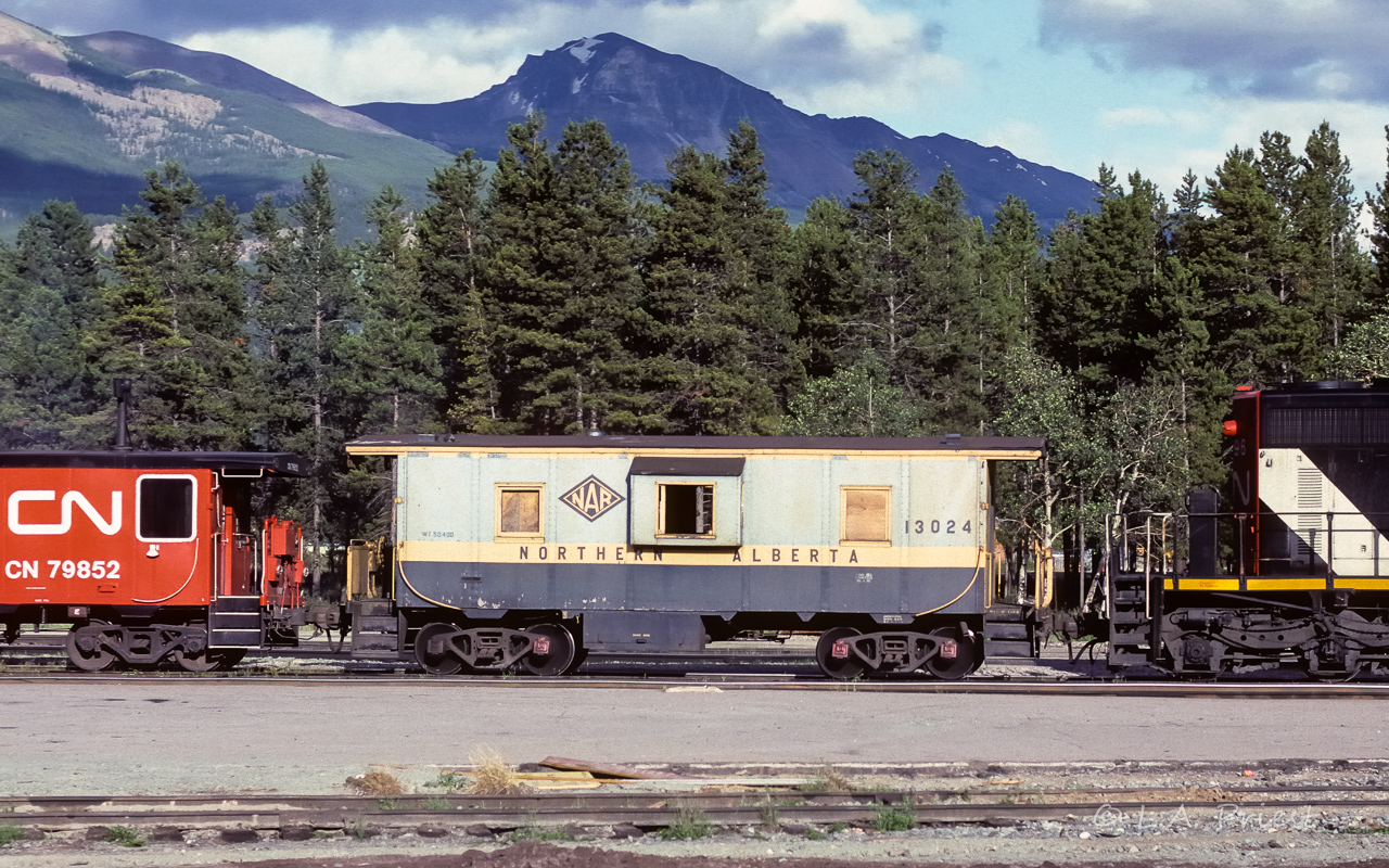 Stopped in at Jasper at suppertime coming home from vacation. I found the 5296 making a move, setting out a BO?, on an eastbound freight. The NAR 13024 was the interesting tag-along at the rear. Finding some info on this caboose required some extra work. I finally found a photo of it on page 17 of volume 2 in the soft cover fold over The Northern Alberta Railways by Colin Hatcher. In the caption, it is mentioned that the 13024 to 13026 were the first NAR caboose to have bay windows applied. Also, that these 3 were built at their own Dunvegan shops in August 1953. In the booklet photo, the 13024 has end ladders going up and then curling down onto the roof, with a nice running board. All have been removed here. Glass in the bay windows has disappeared and the trees behind can be seen. Not a wreck though, plenty re-store-able. Could find no net info on it, thought it may have turned up as a historical item somewhere. Nifty that the NAR paint had not been modified.