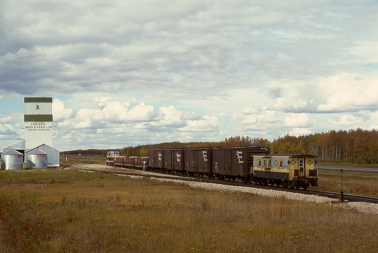 West of Grande Prairie, NAR ran a thrice-weekly wayfreight to Dawson Creek, BC, west Monday, Wednesday and Friday, and returning the next day, almost always with a single GP9.  Here, No. 51 engine 206 on Wednesday 1977-09-21 has three Hart cars of ballast and four empties plus caboose 13006 and is passing the Foster’s elevator at Albright, with 54.8 miles yet to go to Dawson Creek.

Note the green reflectorized target on the switchstand, not centred on the shaft as is common, but offset to the side of the diverging track, an NAR standard that simply makes so much sense.