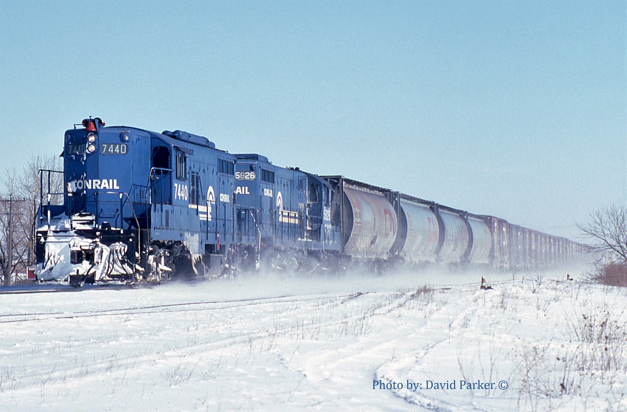 The Conrail St Thomas to Windsor local WQST-4 kicks up the snow as it passes through Tilbury, Ont led by Canada Division GP9 7440 and GP7 5826. Trailing the four CN covered hoppers is the Comber set-off consisting of CN heater cars for Heinz in Leamington.