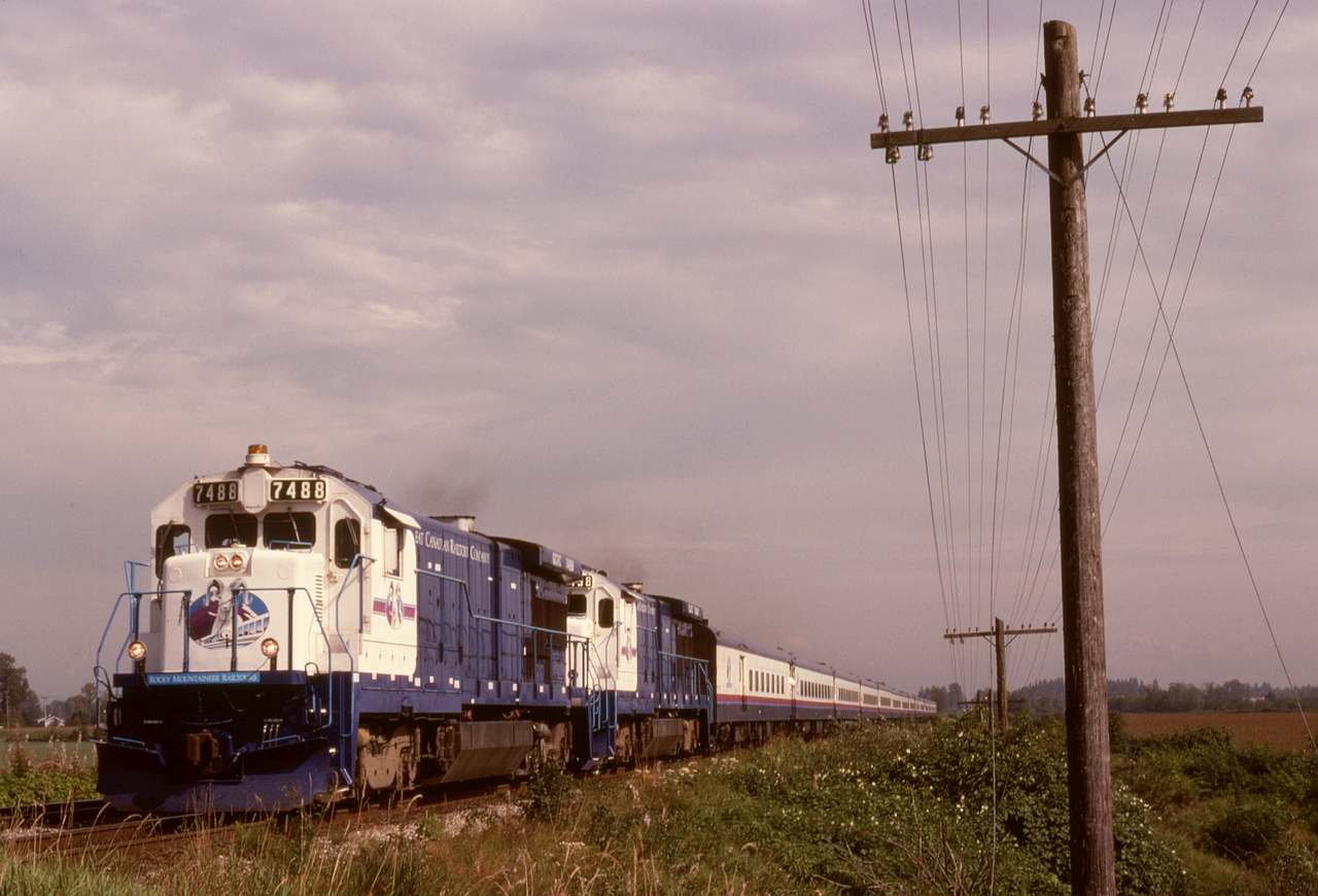 Rocky Mountaineer’s predecessor was the Great Canadian Railtours Company, and they started with a pair of eventually-repainted ex-ATSF GE B37-7 units for power, seen here westbound at 1550 on Wednesday 1992-08-19 with 12 cars in Pitt Meadows and about to cross Kennedy Road then approach the CP Pitt River bridge.

The open farmland on the left side of the photo is now CP’s Vancouver Intermodal Facility, the pole line is long since history, and a CTC crossover is now at the location of the second unit.