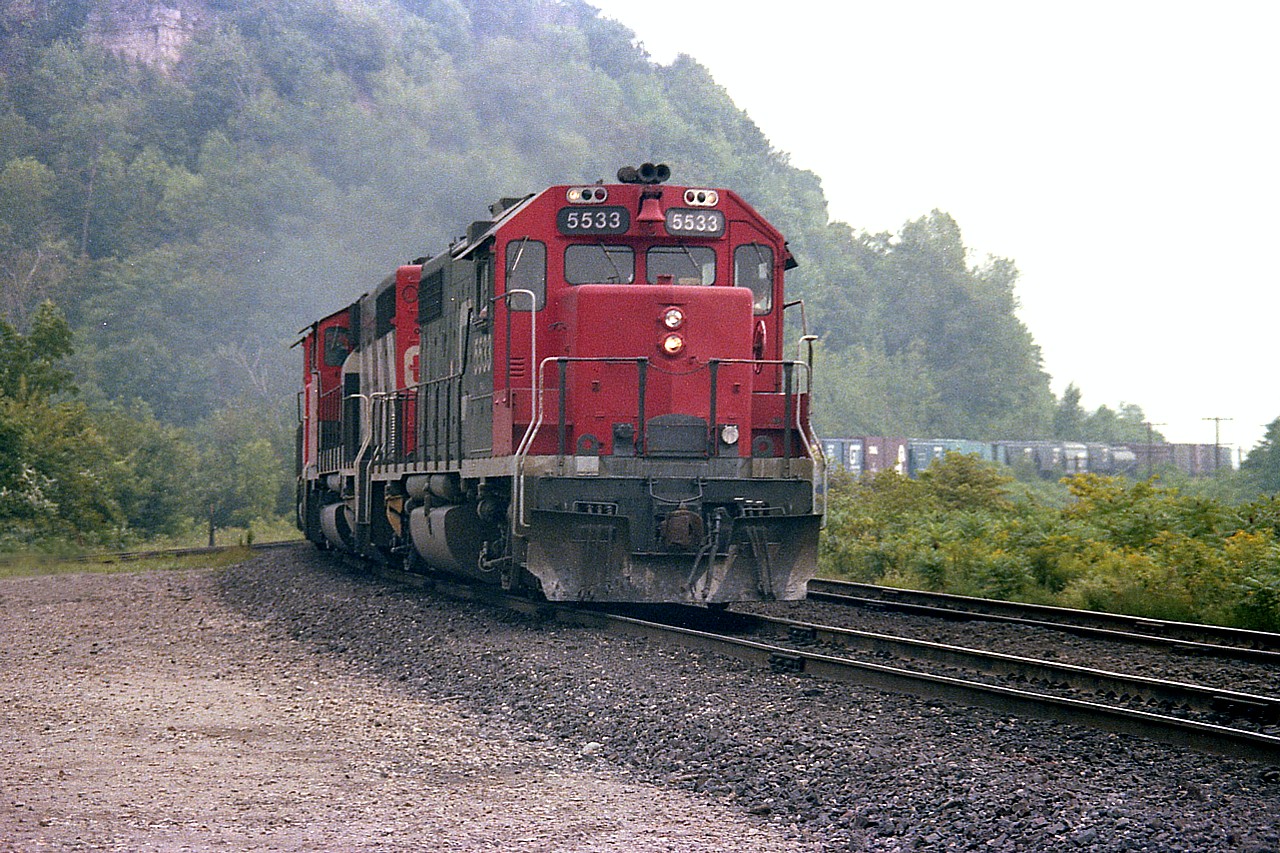 Westbound on the long hill toward Copetown, CN GP38-2 #5533 leads two (unrecorded) GP40-2L widebodies and an SD40, #5038. I've wondered how many units did not sport the "CN" on the nose. The 'lack of' stands out. Photo was taken from by the old station.
CN 5533 became 4733 in 1988 and in 1990 was renumbered to 7532 for yard service.