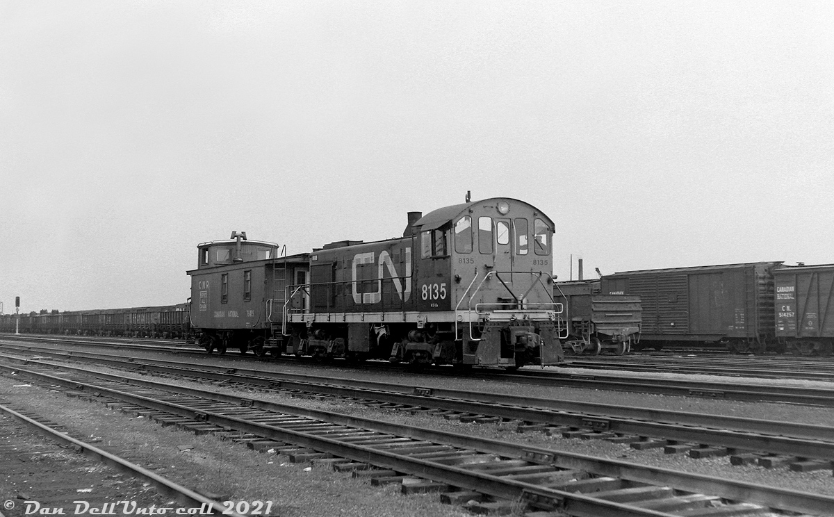 Alco and MLW switchers were typical local and yard power for the steam and early diesel eras, CN and CP both purchased many of the little 660- (S3) and 1000-horsepower (S2, S4) units in the 40's and 50's to replace their smaller steam power. Here, CN S2 8135 sports the brand new "CN" noodle logo and branding, sitting in Danforth Yard with wooden caboose 78429(?) bearing the old "Serves All Canada" wafer logo. Visible in the yard behind is a long cut of "GS" drop-bottom gondolas, perhaps for aggregate service to/from the nearby aggregate industries that were located in the Scarborough area. Also visible is a 40' double door automobile boxcar, and an outside-braced wooden boxcar.

CN's Danforth Yard was once a large freight yard in Scarborough (east end Toronto), at the top of a grade that required pushers in the steam era. It declined in importance after the steam-era due to opening of CN's new modern Toronto (MacMillan) Yard in the mid-60's, and the gradual decline of local rail customers. In its later years it served as home for CN's maintenance of way department and their work equipment. The yard was removed and site redeveloped into housing sometime in the late 90's.

Upon retirement in 1975, CN 8135 was donated to the Canadian Railway Historical Association, Toronto & York Division (CRHA T&Y) and repainted/restored in its original paint and number as CN 7988, and put on display at the CRHA's harbourfront museum near Queen's Quay and Bathurst in Toronto. When the museum was moved out in the late 80's, all equipment was removed and eventually dispersed or disposed of. 7988 apparently had condemned wheels, and was scrapped.

Original photographer unknown, Dan Dell'Unto collection negative (large-format scanned with a DSLR).