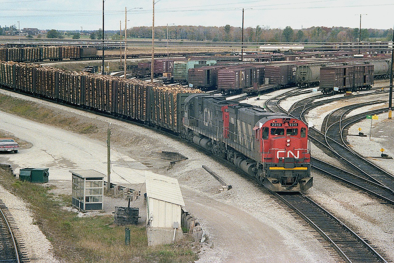 Such an impressive number of wood loads!!   This is the daily CN #431 starting out of Mac Yard as seen from the Hwy 7 bridge over the throat of the yard. It saddens me that a sprawling plant down in Thorold South in the Niagara Peninsula could take loads like this nearly every day at the Ontario Paper Company located there; only to die a slow death and close up a few years ago. Niagara has become an industrial graveyard. In much better days, we see a couple of MLW heavyweights, CN 2313 and 2030, heading out. Yes, I followed this train all the way back to St. Catharines, where I was living at the time. By then, the daylight had faded.