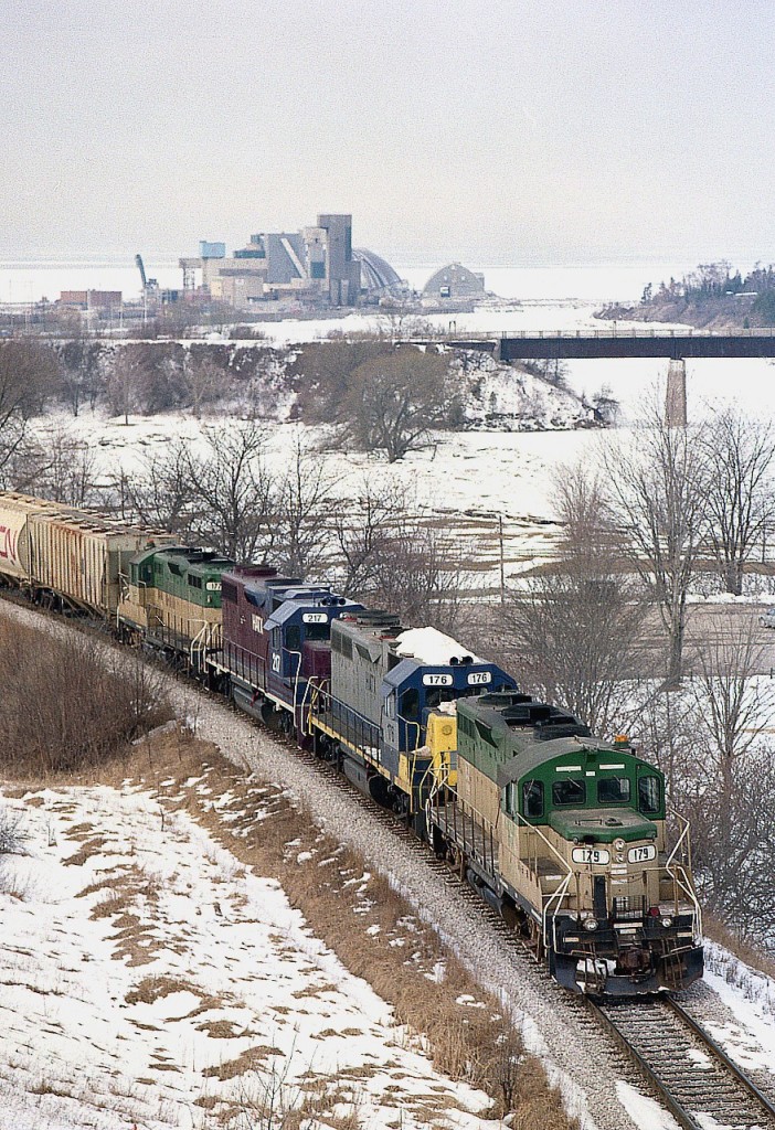 Worth their salt, hauling salt.  It is a stiff grade out of the harbour area where the under-the-lake (Huron)  salt mine is located, and this 4-some has quite the struggle.  Seen are GEXR 179, HATX 176, 217 and GEXR 177. The middle units were leased for awhile thru the winter. One of the mine structures can be seen in the background out on the lake. The bridge over Maitland River once carried the CP line into town, but now is reduced  a walking trail after the rail was pulled up in 1989.