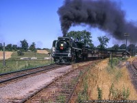 Running out its final miles, Canadian National Railway 6218 rolls an excursion train eastbound through Madoc Junction on the Campbellford Subdivision returning to Belleville after turning on the wye at Anson Junction.  Having just crossed Tuftsville Road, the train passes the <a href=http://www.railpictures.ca/?attachment_id=39373>little station</a> and the siding (designation DB32) in the foreground.  Note the yellow, wooden derail post.  At right lies the Madoc Subdivision.  This excursion would be one of five trips out to Anson Junction and back on July 3 with two trips to follow on July 4 to celebrate the retirement of 6218.<br><br>CN’s Campbellford Subdivision was constructed in segments by different railways over almost three decades.  The earliest portion of the 86.4 mile long line was constructed by the Port Hope, Lindsay & Beaverton Railway from Omemee north west to Lindsay in 1857.  The Grand Junction Railway, originally chartered to build from Belleville to Toronto by looping north through many small communities, was altered to run Belleville to Peterborough with future expansion to Georgian Bay – later cut back to Lindsay.  Only the section to Peterborough would be built under this railway.  Construction began during the 1870s and was completed after many financial issues in 1880.  The final piece of the Campbellford Sub missing at this time was the 13 mile stretch from Peterborough to Omemee, which would be constructed by the Midland Railway of Canada in 1883.  At this time, the PHL&B Ry had been renamed the Midland Railway in 1869, though the company would grow to over four times its size in 1882 with the merger of six struggling railways under its name.  These would include the Midland Railway of Canada; Grand Junction Railway (of Canada); Belleville & North Hastings Railway (see below); Victoria Railway; Whitby, Port Perry & Lindsay Railway; and the Toronto & Nipissing Railway.  The expanded Midland Railway would be leased by the Grand Trunk Railway on January 1, 1884, and finally purchased on April 1, 1893.  The line continued service under the Canadian National Railway banner until abandonment in pieces beginning in 1987 by abandoning Corbyville (mile 3.2) and Peterborough (mile 60.6), and finally the section from Peterborough to Lindsay (mile 86.4) in 1989.<br><br>Originally constructed in 1879 by the Belleville and North Hastings Railway from Madoc Junction (mile 0) to Madoc (mile 14.9), the line was leased to the Grand Junction Railway soon after completion, finally coming under control of the Midland Railway of Canada in 1881.  The Midland Railway extended the line from Madoc to Eldorado at mile 21.69 in 1887, though would close this portion in 1889 due to low traffic.  Service continued after the Midland’s merger with the Grand Trunk and later Canadian National until its last revenue movements in 1979 (5 inbound loads, 12 outbound loads at Madoc) and the line closed to traffic effective January 1980.  CN would be paying to truck loads to/from team tracks at Foxboro (mile 6.54 Campbellford Sub – image below) and Belleville.<br><br>For the two days of July 3rd and 4th, 1971, Belleville was crowded with railfans from all over, many from the USA familiar with 6218 trips on Central Vermont and Grand Trunk Western lines.  A ceremony was held at Belleville station on the 4th bidding farewell to 6218 before its final departure, well documented in the Upper Canada Railway Society’s July 1971 newsletter (link below).<br><br>An excerpt from the UCRS article:<br>“6218 herself was in pristine condition for her final hours of glory.  She had been restored to her World War II appearance, complete with rectangular herald on the tender coal bunker, smoke deflectors (or "elephant ears") around the smokebox, a glossy black paint job complete with white striping on the running boards and cab of the engine and on the tender, and yellow numerals on the cab sides.  The wheels and drivers on engine and tender were painted their usual white...The highways and byways from Belleville to Anson Junction were dotted with cars with many United States license plates, as people came from far and near to see 6218 make her last run on this weekend...A stirring eulogy to 6218 was given by Mr. O.S.A. Lavallee of Montreal.  At the conclusion of the eulogy, the Duke of Edinburgh Pipe Band played "Auld Lange Syne".  There was now a hush in the crowd, as people stood waiting, cameras and tape recorders at the ready.  The band played a second time.  After what seemed an eternity, out of the east a plume of black smoke arose.  6218 then came screaming down the yard, through the leads and past the station and the assembled crowd, whistle blowing, doing an estimated 60 per.  She disappeared into the sun in the west, and it was all over.”<br><br>The full UCRS article covering the final trips of 6218 can <a href=https://railwaypages.com/upper-canada-railway-society-ucrs-and-its-publications>be FOUND HERE</a> in newsletter 306: July 1971.<br><br>More Campbellford/Madoc Sub images:<br><a href=http://www.railpictures.ca/?attachment_id=43376>Lindsay, Bruce Lowe, June 1964</a><br><a href=http://www.railpictures.ca/?attachment_id=44920>Foxboro, Doug Page, June 1964</a><br><a href=http://www.railpictures.ca/?attachment_id=39373>Madoc Junction, Arnold Mooney, July 1976</a><br><a href=http://www.railpictures.ca/?attachment_id=29999>Madoc, Arnold Mooney, July 1976</a><br><a href=http://www.railpictures.ca/?attachment_id=15760>Hastings, Steve Danko, May 1977</a><br><a href=http://www.railpictures.ca/?attachment_id=14501>Peterborough, Eric May, 1979</a><br><a href=http://www.railpictures.ca/?attachment_id=44270>Stirling, Arnold Mooney, July 1979</a><br><a href=http://www.railpictures.ca/?attachment_id=45655>Stirling, Arnold Mooney, July 1979</a><br><br><i>James C. Herold Photo,  Jacob Patterson Collection Slide.</i>
