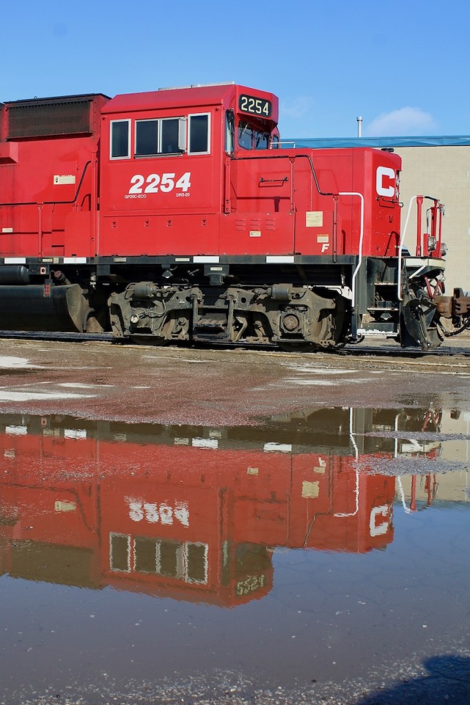 Area "H" reflections. After spending a hour along the Area H spur in Etobicoke on Saturday, all I could think of was the scale model creations of layout maker Lance Mindheim. He is well know for his real to life industrial spur HO scale switching layouts, such as the Miami spur and Los Angeles spur. These spurs along with CP's Area H consist of numerous rail served local industries, (some abandoned). Rails imbedded in the roads and parking lots they encounter as well as along active roadsides. While this image doesn't do justice to most of that, just watching the crew do their work left me looking forward to my next visit. Unfortunately the local has to back southward down the spur, making decent sunny day shots hard to come by, at least with the power leading.  Nevertheless the area is worth a visit, typically Tuesday, Thursday and Saturday. Here the train is seen reflecting in a puddle deep along the spur as they switch out tank cars.