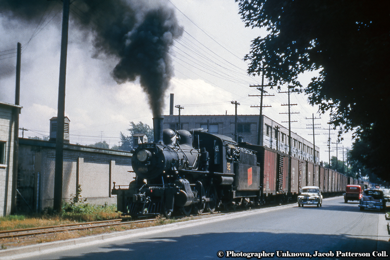 Returning from Tilsonburg with a string of mostly 40 foot boxcars, Canadian National Railway E-10-a, 2-6-0 Mogul, 92 rolls alongside Clarence Street in Brantford, just about to cross Nelson Street.  Behind the train is the large H. E Mott Company Limited building on the north east corner of Clarence and Wellington Streets, a site connected to Brantford's agricultural heritage.Originally built in the 1870s for the J. O. Wisner Son & Co. (founded 1872) manufacturing fanning mills and seed drills, the company amalgamated with the Massey-Harris Company in 1892.  At that time, the Verity Plow Company, originally of Exeter, Ontario, relocated to Brantford in the former Wisner facility.  Verity too would become connected to Massey-Harris during the late 1890s, and the building would be sold to the Goold, Shapley & Muir Co. who manufactured farming implements with a focus on gasoline engines, used mainly in powering tractors.  Facing financial difficulties during the 1930s, the company finally succumbed to the Great Depression in 1934, at which time, the H. E. Mott Company Limited was founded, assuming control of the property until 1958, when the company relocated to a spot on Wadsworth Street.  Further information is not noted, however the building was demolished on August 31, 1976.  Information from Brantford Historian, Jack Jackowetz.Built by the Canadian Locomotive Company in 1910 for the Grand Trunk Railway as E12 class number 1017.  It would be renumbered to CNR 919 in 1923, and to CNR 92 in 1951.  92 is one of the surviving CNR Moguls in the United States, currently awaiting restoration at the Wilmington & Western Railroad in Wilmington, Delaware.Original Photographer Unknown, Jacob Patterson Collection Slide.