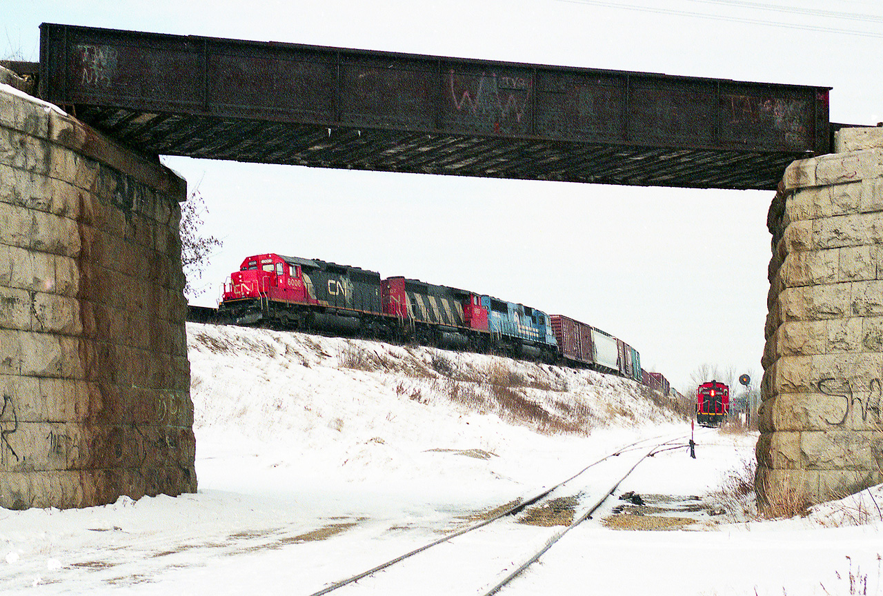 At Brant Junction the Burford spur heads south to the old industrial area of Brantford, and the Dunnville Sub to Caledon and Fort Erie passes overhead on an old stone and iron bridge.  A westbound freight led by CN6006 and a Contrail loco passes by on the Dundas sub, while the switcher waits for clearance to return to Brantford yard, 8/10 mile west.  February 1994