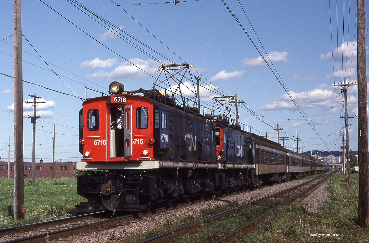 The "Air conditioning" is on full blast and a friendly wave from the motorman of an afternoon Westbound commuter train powered by a pair of English Electric boxcabs at CN Jct D L'Est in Montreal.