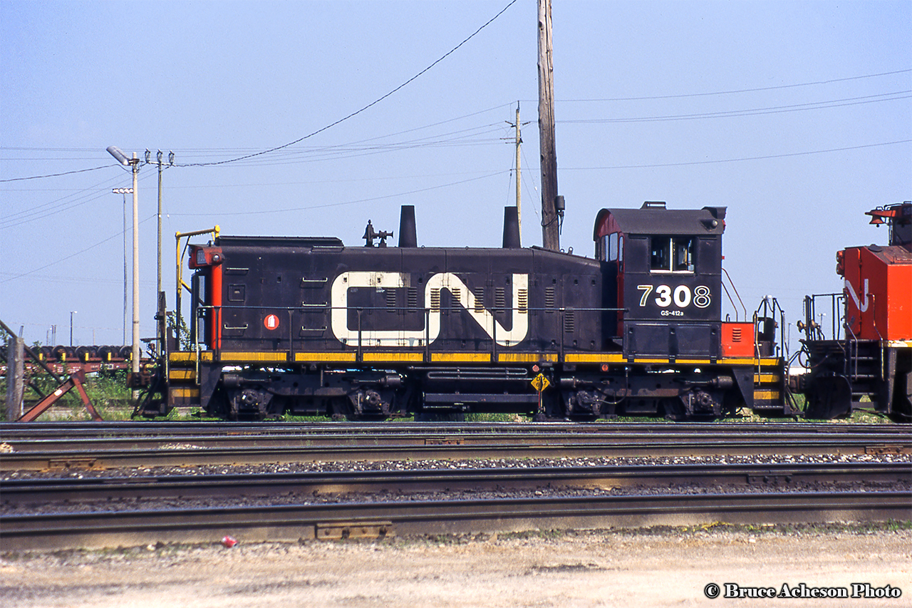 CN SW1200RSu 7308 sits near the shop at Mac Yard coupled to M420 3522.  Built in 1960 as CNR 1373, the pup was rebuilt in 1987 to 7308 and retired in March 2000.  From CN, the unit was sold to Canac and later to Savage Services, receiving their paintjob around 2013 becoming SVGX 7308.  Barely in frame, 3522 originally CN 2522, would be retired in March 1998 and sold a few months later to National Railway Equipment in Silvis, Illinois.  It would be picked up by the Cape Cod Central Railroad becoming their 2000 for a couple of years before returning to Canada and heading for the prairies as Great Western Railway 2000.  The GWR retired it’s MLW fleet in recent years, with the 2000 moving east to Manitoba, now operating on the Keewatin Railway as their 2404.
