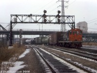 Light snow falls at Don as CN S2 8136 works the P500 service track, shortly after meeting a southbound CP transfer freight lead by RSD17 8921 and <a href=http://www.railpictures.ca/?attachment_id=33301><b>caboose 438811</b></a> on the tail end. Note the sign on the old signalbridge: This is the northeasternmost point where the downtown Toronto Terminals Railway trackage begins/ends, at CP's Belleville Sub (Don Branch, left track) and CN's Bala Sub (center track). CP and CN interchanged cars further south at their <a href=http://www.railpictures.ca/?attachment_id=47272><b>Cherry Street</b></a> yards. The old S. McCord cement plant looms in the background, with parked cement mixers visible under the Queen Street bridge to the right.
<br><br>
Today's consist is a CP 50' boxcar (42526, assigned auto parts service), a BASF Wyandotte chemical tank car, a green CPI 85000-series newsprint service boxcar, a pair of tanks, and an old steel <a href=http://www.railpictures.ca/?attachment_id=33806><b>CN ice reefer</b></a>. CN S2 8136, built by MLW in 1949, was one of the handful of yard units assigned out of Spadina Roundhouse for local and switching dutes, and would be retired a few months later in October.
<br><br>
Soon, a southbound freight lead by CN SW1200RS units 1320 and 1213 would put in an appearance: <a href=http://www.railpictures.ca/?attachment_id=39454><b>http://www.railpictures.ca/?attachment_id=39454</b></a>.
<br><br>
<i>Original photographer unknown, Dan Dell'Unto collection slide.</i>
