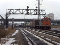 Light snow falls at Don as CN S2 8136 works the P500 service track, shortly after meeting a southbound CP transfer freight lead by RSD17 8921 and <a href=http://www.railpictures.ca/?attachment_id=33301><b>caboose 438811</b></a> on the tail end. Note the sign on the old signalbridge: This is the northeasternmost point where the downtown Toronto Terminals Railway trackage begins/ends, at CP's Belleville Sub (Don Branch, left track) and CN's Bala Sub (center track). CP and CN interchanged cars further south at their <a href=http://www.railpictures.ca/?attachment_id=47272><b>Cherry Street</b></a> yards. The old S. McCord cement plant looms in the background, with parked cement mixers visible under the Queen Street bridge to the right.
<br><br>
Today's consist is a CP 50' boxcar (42526, assigned auto parts service), a BASF Wyandotte chemical tank car, a green CPI 85000-series newsprint service boxcar, a pair of tanks, and an old steel <a href=http://www.railpictures.ca/?attachment_id=33806><b>CN ice reefer</b></a>. CN S2 8136, built by MLW in 1949, was one of the handful of yard units assigned out of Spadina Roundhouse for local and switching dutes, and would be retired a few months later in October.
<br><br>
Soon, a southbound freight lead by CN SW1200RS units 1320 and 1213 would put in an appearance: <a href=http://www.railpictures.ca/?attachment_id=39454><b>http://www.railpictures.ca/?attachment_id=39454</b></a>.
<br><br>
<i>Original photographer unknown, Dan Dell'Unto collection slide.</i>