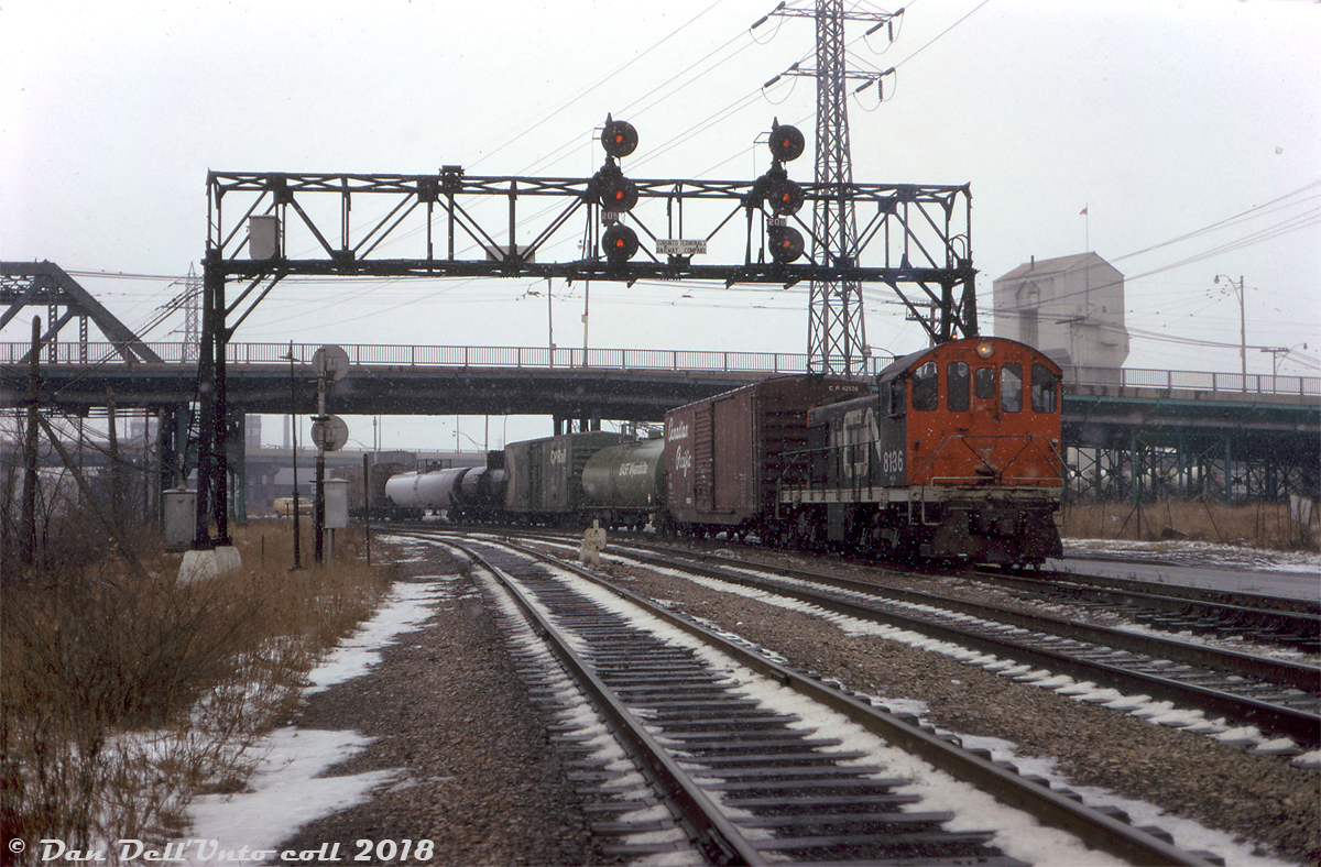Light snow falls at Don as CN S2 8136 works the P500 service track, shortly after meeting a southbound CP transfer freight lead by RSD17 8921 and caboose 438811 on the tail end. Note the sign on the old signalbridge: This is the northeasternmost point where the downtown Toronto Terminals Railway trackage begins/ends, at CP's Belleville Sub (Don Branch, left track) and CN's Bala Sub (center track). CP and CN interchanged cars further south at their Cherry Street yards. The old S. McCord cement plant looms in the background, with parked cement mixers visible under the Queen Street bridge to the right.

Today's consist is a CP 50' boxcar (42526, assigned auto parts service), a BASF Wyandotte chemical tank car, a green CPI 85000-series newsprint service boxcar, a pair of tanks, and an old steel CN ice reefer. CN S2 8136, built by MLW in 1949, was one of the handful of yard units assigned out of Spadina Roundhouse for local and switching dutes, and would be retired a few months later in October.

Soon, a southbound freight lead by CN SW1200RS units 1320 and 1213 would put in an appearance: http://www.railpictures.ca/?attachment_id=39454.

Original photographer unknown, Dan Dell'Unto collection slide.