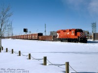 CP GP38-2 3105 has just departed Winnipeg Yard and crossed McPhillips Street crossing, heading up CP's Winnipeg Beach Sub for the trip east out of town for Selkirk, Manitoba. In tow is a single 65' gondola followed by a long cut of CN "Buffalo Boxcars" interchanged to CP, all heading to their final fate at Mandak Metals to be cut up for scrap. <br><br> The old 40' boxcar was the standard for transporting grain in Canada for decades until the introduction of covered hoppers, and the build-up of large fleets by CN, CP, and the provincial and federal governments in the 70's and 80's to modernize Canadian grain transportation. Unfortunately, not all branchlines were up to handling those new 100-ton cars, and the aging 40- and 50-ton 40' boxcars, shrinking in number, still soldiered on on many prairie branchlines whose light rail couldn't handle heavier cars. One line in particular that posed a problem was the CN's Hudsons Bay line north to the port of Churchill, Manitoba, that was restricted from using covered hoppers but home to an important government arctic seaport. <br><br> Often it was more cost-effective for railways to overhaul the aging boxcars rather than upgrading unprofitable grain-handling branchlines, and governments were willing to invest in new fleets and overhaul programs to help the railways move Canadian grain to market. In the mid-80's, CN undertook a rebuild program using provincial and federal government funds to overhaul a fleet of 40' boxcars for continued service transporting grain to the port in Churchill. Hundreds of these refurbished cars were repainted in a special livery with Canada and Manitoba government lettering (including Manitoba's provincial buffalo logo, hence the nickname). They were restricted from interchange service, and lettered "For Thunder Bay and Churchill grain service only": in the warmer months they shuttled grain from Manitoba and parts of Saskatchewan up the Hudson Bay line to the port in Churchill, and in the colder months when that port was closed, they headed east to the lakehead elevators in Thunder Bay. <br><br> It's interesting to note they were all rebuilt with new 8' doors, but kept their old 6' door openings behind them (likely to accept standard grain doors that were sized to fit 6' doorways). <br><br> Dwindling fleets of 40' boxcars continued to haul grain for CN and CP into the 90's, but quickly shrinking in number due to age and as prairie branchlines were either upgraded or outright abandoned. Prior to the takeover by Omnitrax, CN lifted the ban on covered hoppers on the line to Churchill in late 1996, and that spelt the end of the Buffalo Boxcar fleet, and the final end to hauling grain in 40' boxcars in Canada. Many were rounded up and sent to Mandak Metals in Selkirk MB for scrapping, where the cut following CP 3105 will ultimately end up. <br><br> <i>Bill Linley photo, Dan Dell'Unto collection slide.</i>