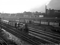 A steam-era view from the Spadina Avenue bridge looking west: CP RS10 8566 leads an inbound passenger train into downtown Toronto bound for Union Station, passing CN's Bathurst Street freight yards (full of the typical 50's freight car mix dominated by 40' boxcars and ice reefers, most sporting CN's maple leaf logo). An old 40' flatcar loaded with wheels is visible in the middle of the yard. Nearby, CN S2 8133 sits on one of the yard leads between switching duties.

The ever-present Front Street runs across the background, elevated above the yard, and populated by factories and houses that largely vanished in the following decades (a small gathering of historic houses along Draper Street remain today). The old <a href=http://www.railpictures.ca/?attachment_id=38487><b>Bathurst Tool</b></a> building is visible on the far left. Judging by the sun angle and snow on the ground, this may be an evening winter shot.
<br><br>
<i>Original photographer unknown, Dan Dell'Unto collection negative.</i>