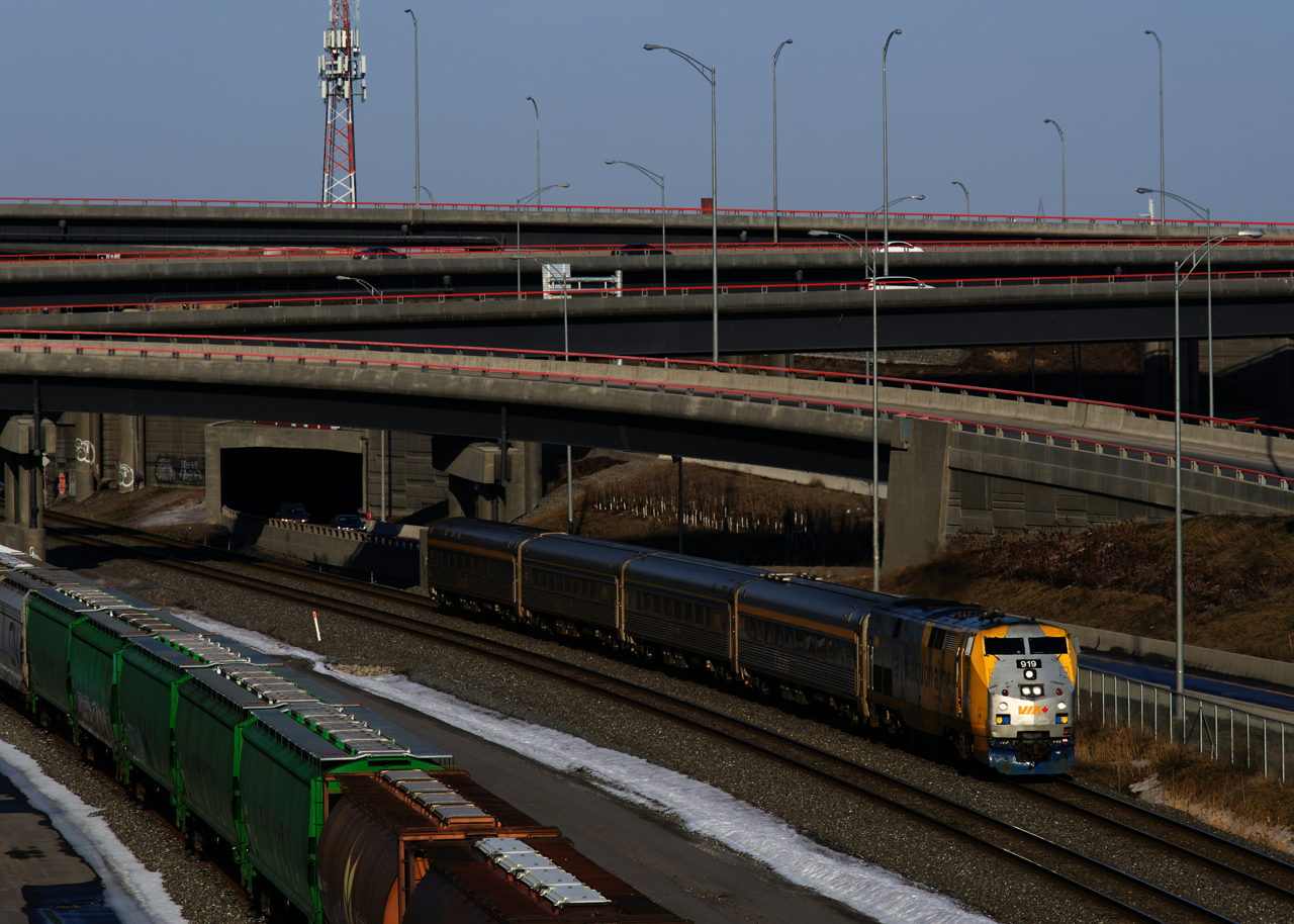 VIA 37 has VIA 919 and four HEP cars as it passes cars parked on Track 29 of CN's Montreal Sub. VIA 919 has a blue plow, whereas most of VIA's wrapped Genesis units have a darker plow.