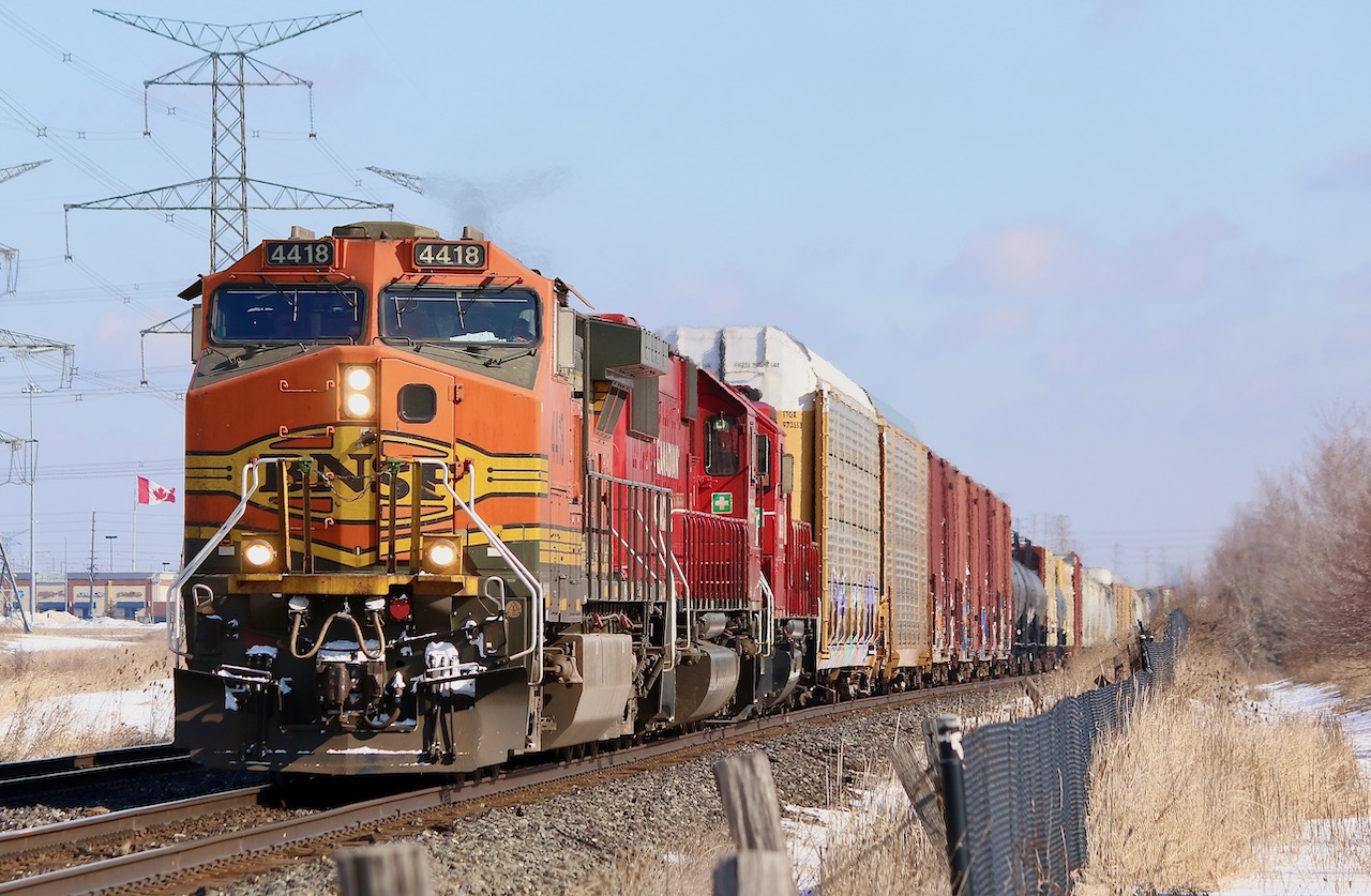 Foreign leaders on westbounds out of Toronto certainly are not as common as on eastbounds. It was nice having the cloud cover clear just before 141 arrived with BNSF Dash-9 4418 in the lead. trailing is a former SOO SD60 and a CP GP38, while an AC4400 is hiding mid train as DPU. Not sure why local T14 ran the north track to Hornby this morning only to be forced to sit it out at Hornby west for a half an hour to wait for 141 to finally pass on the south, then T14 finally got the light to back into Hornby yard. Here 141 is seen leaving Lisgar in the distance , while  Canadian flag flaps in the wind at a local plaza.