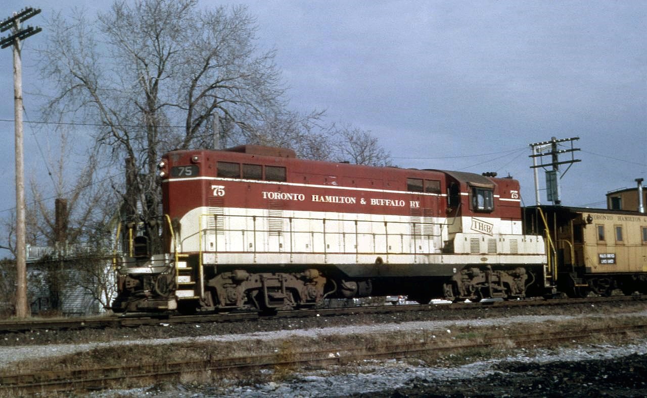 The Intruder Within - #75 and Van #70 heading west on the CNR.  The pair have just crossed King Street, the CN Station would be to the east of the photographer.  By the time this photo was taken, TH&B had enjoyed running rights into Port Colborne for more than 40 years.  When they acquired the running rights in the mid-1920's, Port Colborne was one of the top car load origins in the Province, and TH&B got their share without having to lay down a single rail.  Van #70 shown here is in the TIGER-CATS colour scheme, and survives to this day at the Toronto Railway Museum - repainted in the earlier Red colour scheme.  Thanks Steve for the help here !