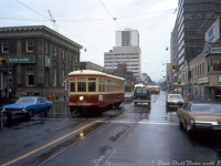 A rainy day in October 1973 finds TTC Peter Witt streetcar 2766 deadheading through mid-town Toronto, heading westbound on St. Clair Avenue crossing Yonge Street. The regular "Tour Tram" routing that 2766 was restored for months earlier ran around downtown streetcar trackage, so 2766 could be running a private fantrip coming from the nearby St. Clair subway station. A westbound PCC operating in regular service on the St. Clair route follows a few cars behind, and another PCC can be seen turning into St. Clair station's loop, probably a westbound from Eglinton Loop <a href=http://www.railpictures.ca/?attachment_id=32380><b>via Mount Pleasant</b></a>/St. Clair.
<br><br>
Large office towers have since replaced both the TD Bank building at the northeast and the Super Save Drug Mart at the southeast corners. License plate afficionados, note the brand new original A-series license plate on the right: 1973 was the first year Ontario plates weren't replaced on a yearly bases (rather, they required annual sticker updates to be valid).
<br><br>
<i>Original photographer unknown, Dan Dell'Unto collection slide.</i>