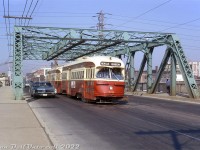 <b>Above the Don:</b> TTC A7-class PCC 4462 is operating on the busy Queen streetcar route, MU'ed with an A12-class ex-Cleveland PCC (4675-4699 series). Both are crossing from downtown into the Riverdale part of Toronto, over the old Queen Street bridge spanning the Don River, the CN-CP rail corridor, Don Valley Parkway and Bayview Avenue. Built in 1911, this truss bridge spanned the river and eliminated an at-grade crossing with the rail lines below, and continues to handle automobile and King, Queen, McCaul and Kingston Rd. streetcar traffic today.<br><br>Railway related note: the Ace Warehouse Company building to the right (behind the bridge) was once served by a rail spur off CN's Bala Sub that crossed Bayview Avenue.<br><br>Automobile enthusiasts: I spy a mid-60's Pontiac!<br><br><i>Original photographer unknown, Dan Dell'Unto collection slide.</i>