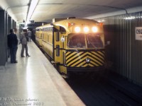 Streetcars in the subway? Sort of: a group of downtown businessmen wait paitiently for the next subway train as TTC work cars RT-15 and RT-14 pass through the station northbound on the University line, taking on no passengers. This may be an evening shot, as that's when subway work cars usually came out to peddle their trade across the system.<br><br>After two decades of prowling the TTC's streetcar network above-ground, two 4400-series (A7-class) PCC streetcars were converted into subway work cars in 1970 for railgrinder service (4446 and 4410 to RT-14 and RT-15, respectively) to replace older equipment. They traded in their trolley poles for 3rd rail pickups, and scraper bricks were installed on their trucks to provide the grinding (a similar modification was done to PCC's W-30 & W-31 for the streetcar network).<br><br>In terms of body work, the cars were mated back-to-back with rear doors to pass from one car to the other, carbody modifications included plating over some windows, two-level doorways at the front (one at the regular lower level, the other at the higher subway platform level), class lights and extra bright headlights mounted where the destination signs were. The right-side middle doors were plated over, and an extra single door was cut into the left side of each car for alternate platform access. Brackets were added at the top right of the cars for installation of Identra Coils to trigger the platform signs.<br><br>Other photos hint that the two cars lasted into the early 1980's before they were retired and disposed of, but similar looking yellow PCC work cars W-30 & W-31 survive today on at the HCRY.<br><br><i>J. W. (Bill) Vigrass photo, Dan Dell'Unto collection slide.</i>
