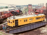 On the CP E&N turntable at Victoria on Saturday 1976-05-01, Sperry car SRS 129 (which dates from 1925 as Lehigh Valley 29) is rotated in a time warp of similar-age CP facilities and equipment, most notably the 1920s Industrial Works 100-ton auxiliary crane 414326.

<p>In the distance above the centre of the car is the simple 1972 concrete block depot at mileage 0.8 which replaced the downtown depot at mileage 0.0 at Store Street.