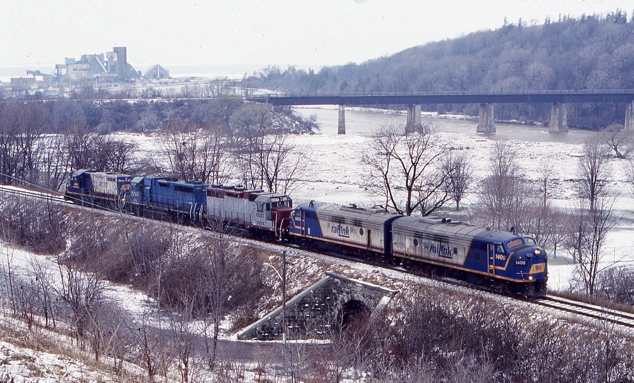 This is probably the most interesting and colourful consist I ever photographed on GEXR train 581. After lifting GP 9 4001 from the shop, the train  now has just finished backing a cut of salt hoppers to the load out at the harbour. Power this day is a pair of ex VIA FP9’s, a former DRG&W GP35, now a CEFX GP38, a LLPX GP38, formerly an IC GP40 and  a former SP GP9. The salt company can be seen well In the distance, as well as CP’ s abandoned  Goderich subdivision  crossing the river in the foreground.