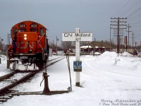 <i><b>Snowy winter branchline railroading</b></i>: CN GP9RM 4103 and another unit come off the Midland Sub at Midland Junction in Orillia, entering Mile 86.1 of the Newmarket Sub south of Front Street South crossing. A blue-painted CN billbox is fastened to the station name sign post, with a switch broom at arm's length away to clear out any snowy switch points encountered. VIA/CN's old Orillia Station can be seen in the distance, and behind that some OCS work cars on the other leg of the wye.
<br><br>
Once reaching from Lindsay to Midland, by this time the Midland Sub only ran from Mile 42.7 (Orillia) to 75.2 (Midland), and was one of the many small southern Ontario branchlines on borrowed time. Following dwindling traffic, the line was approved for abandonment in sections during 1994 and 1995 and lifted, followed by CN abandoning the Newmarket Sub north of Barrie (Mile 63) through Orillia to Longford (Mile 93.0) in September 1995, and removing it in 1997-98. Only the Orillia Station, restored in 1989 but recently put up for sale by the city, remains as a reminder of the railway's presence in town.
<br><br>
An <a href=https://otc-cta.gc.ca/eng/ruling/70-r-1995><b>abandonment filing</b></a> noted service on the Midland Sub was provided five days per week from a Barrie-based wayfreight, with traffic mainly being inbound loads of plastics and outbound loads of aggregate from Uhthoff.
<br><br>
<i>Barry Schroeder photo, Dan Dell'Unto collection slide.</i>